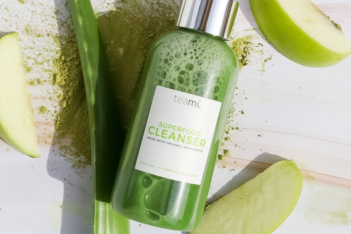 Teami Superfood Cleanser bottle on table with apple and aloe vera