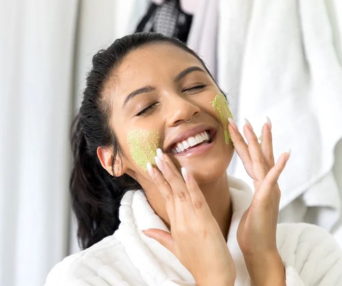 happy young woman applying teami detox mask on her face