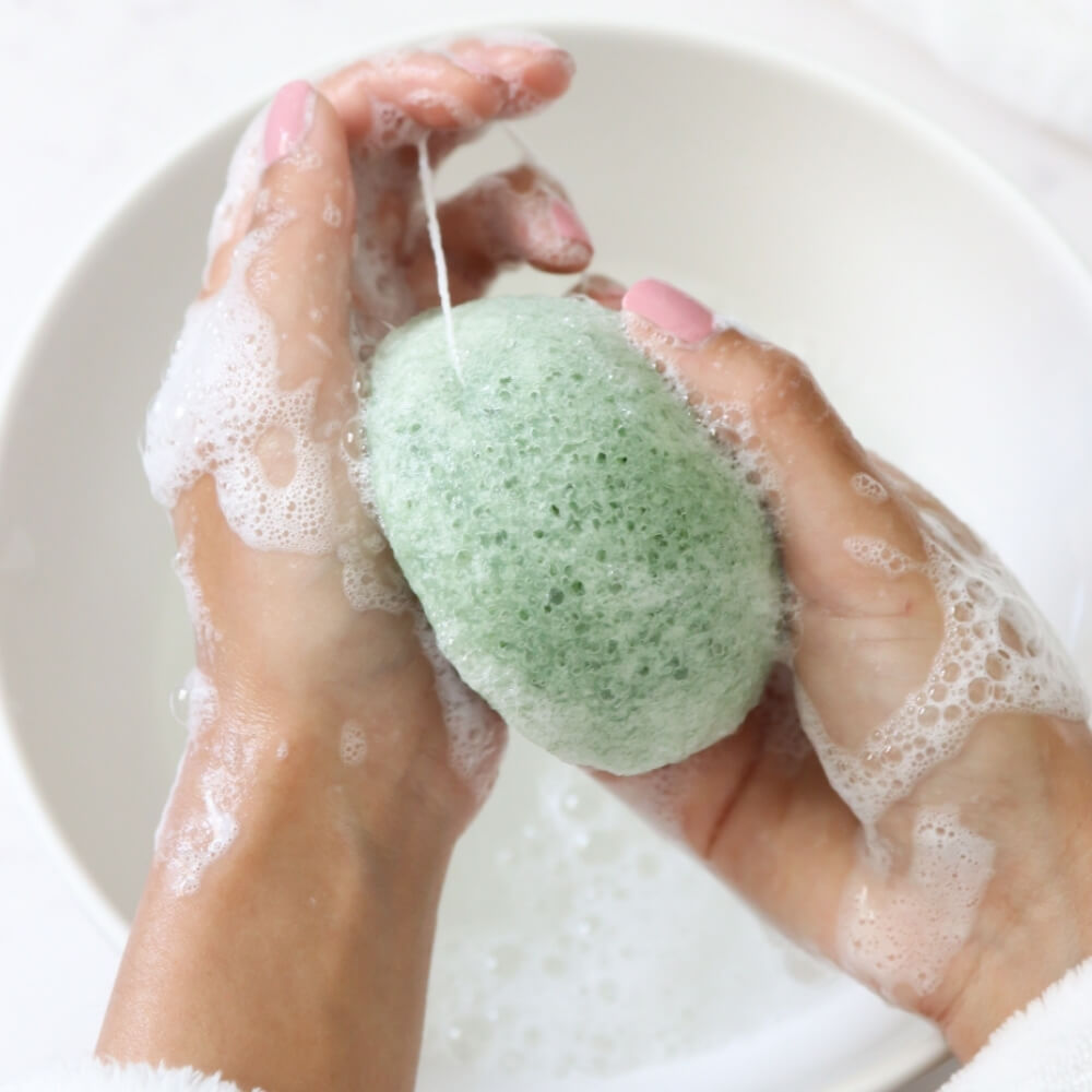Women with soapy hands using Teami tea infused konjac sponge over sink