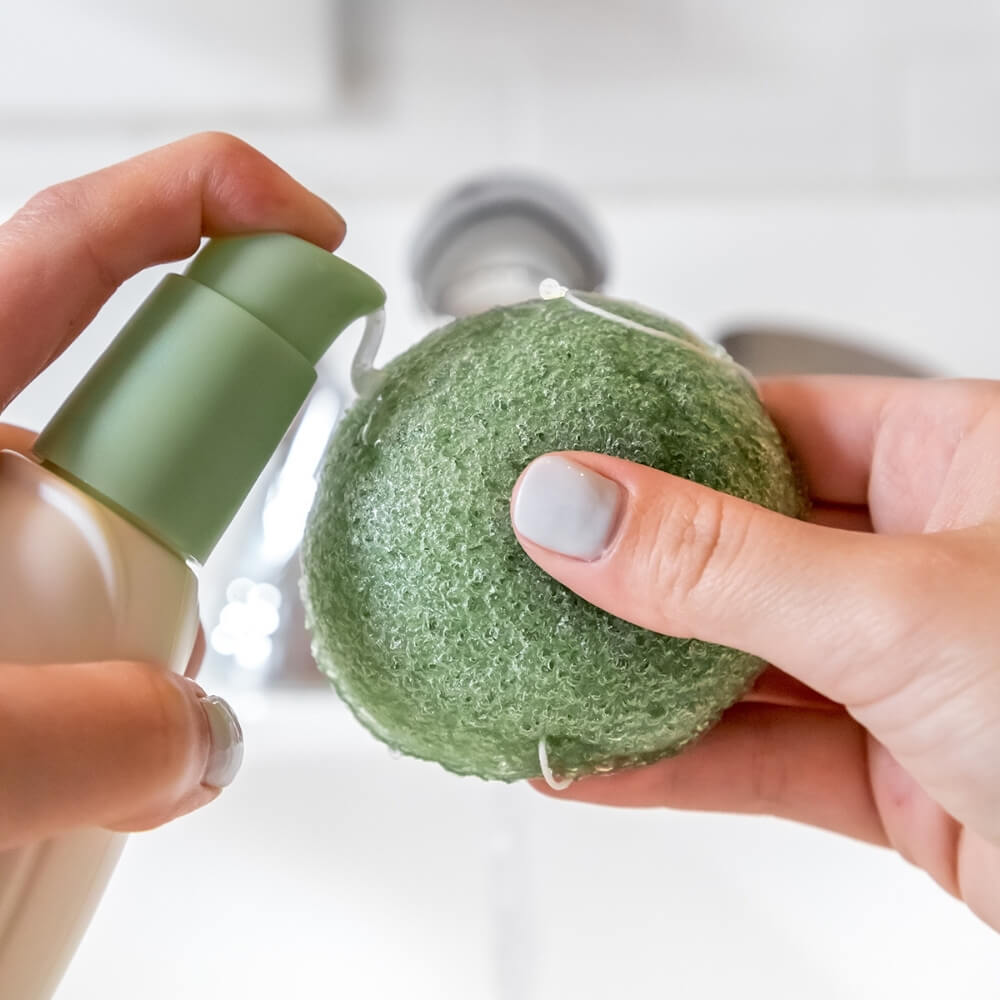 Hands using pump bottle to add moisteriser to Teami tea infused konjac sponge
