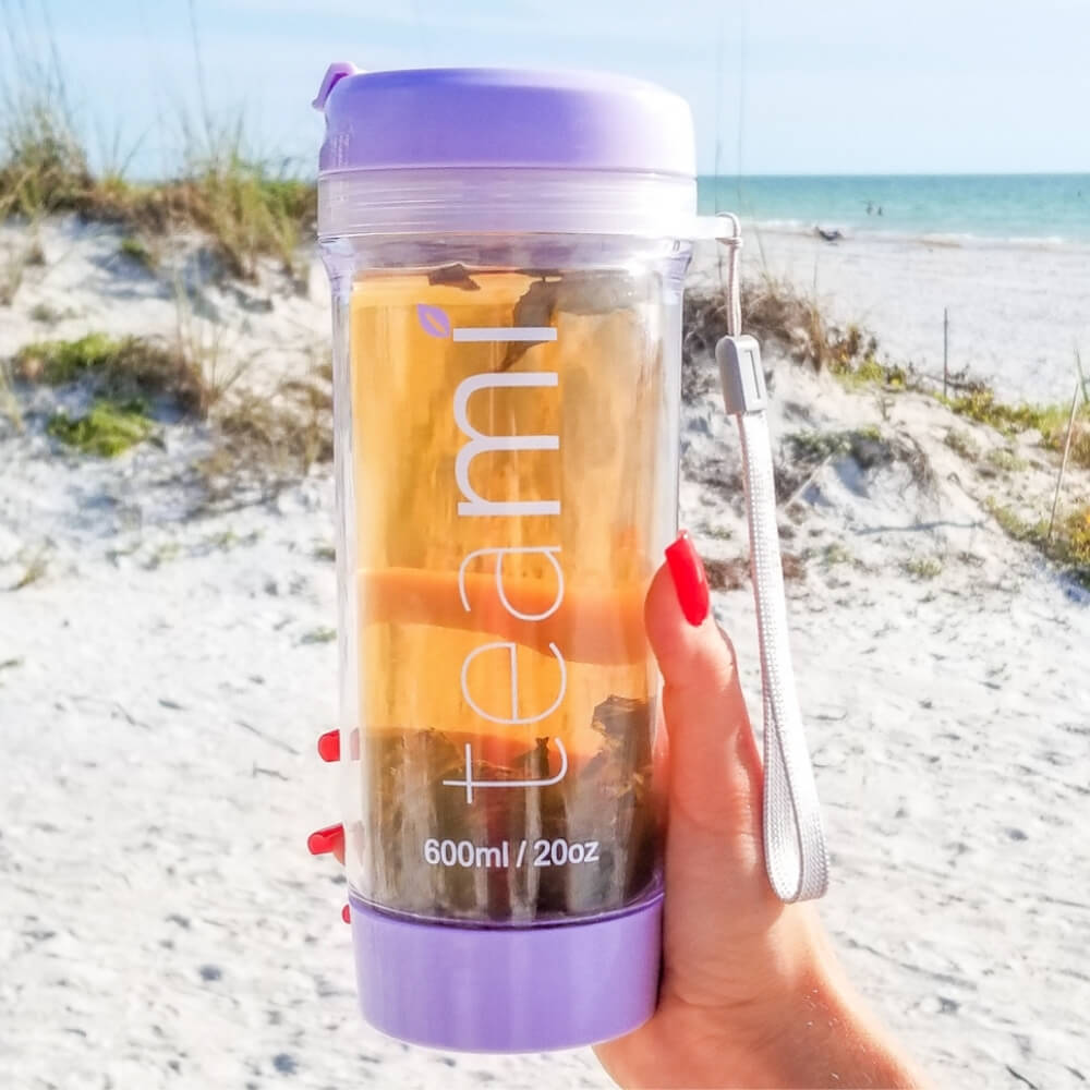 girl holding purple teami tea tumbler on beach