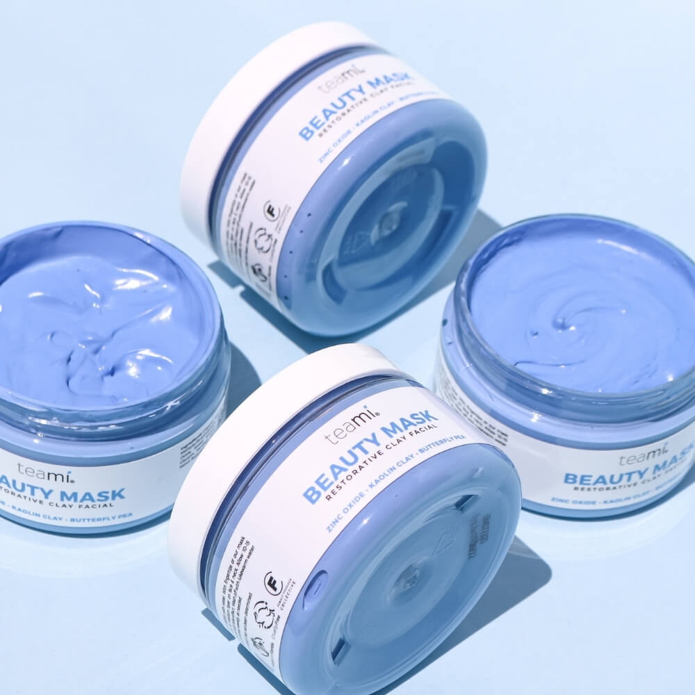 Four tubs of Teami beauty mask with zinc oxide, kaolin clay and butterfly pea on blue background