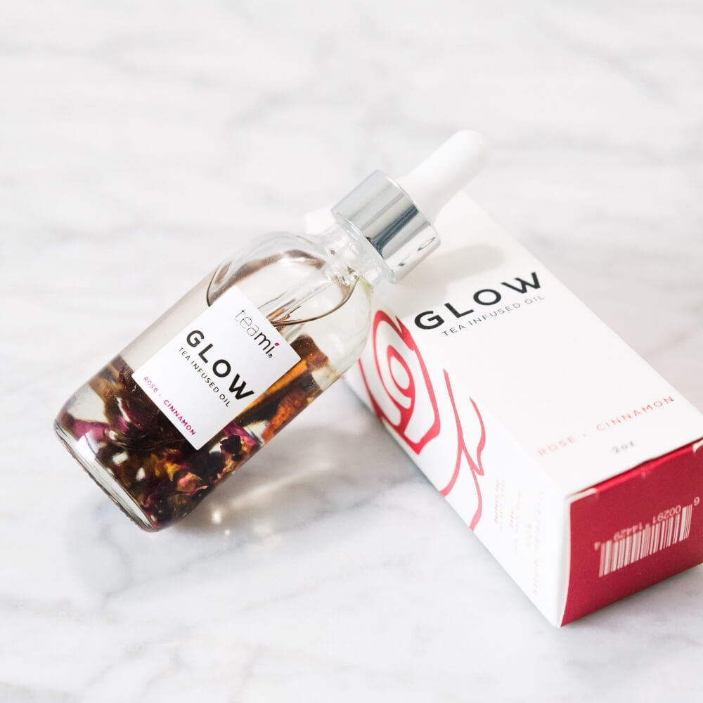 Teami glow oil with rose and cinnamon leaning against packaging
