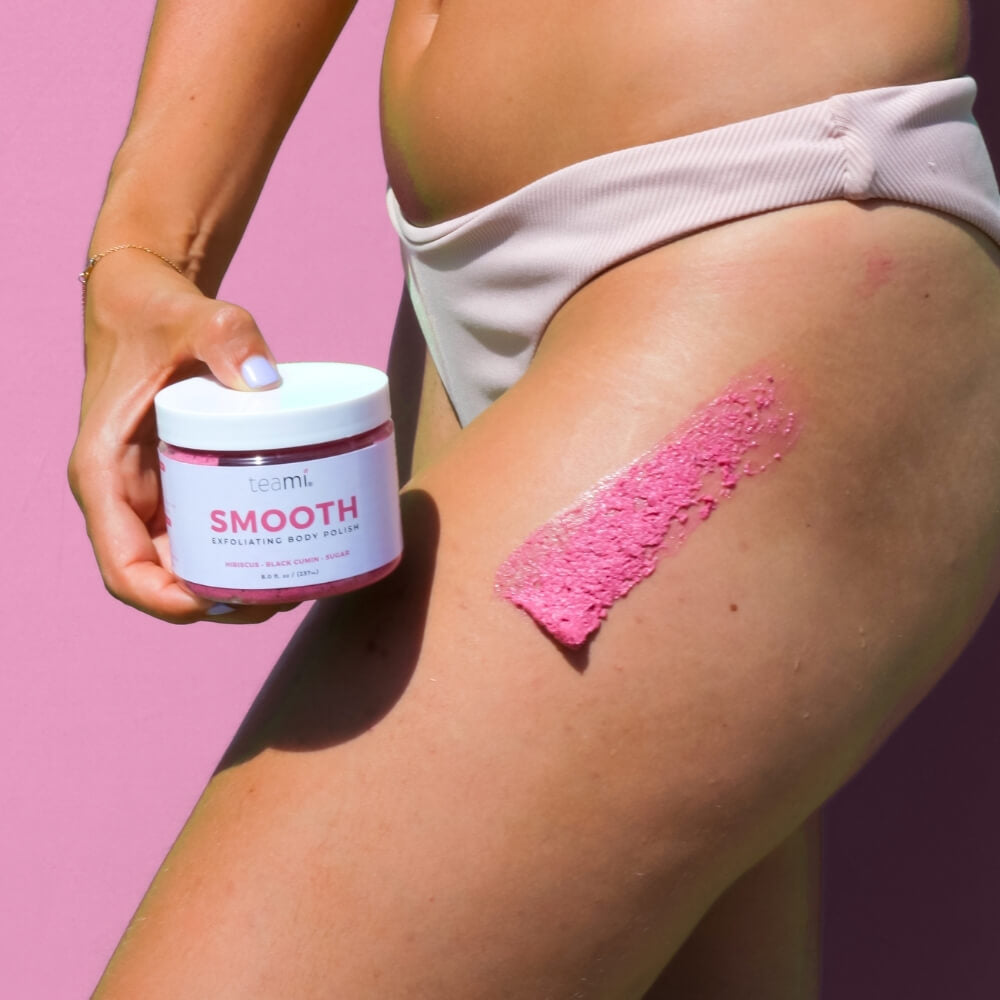 Woman holding pot of Teami smooth body polish pot next to her leg with product applied
