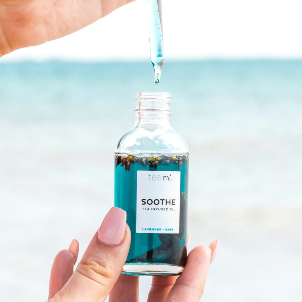 Person using dropper of Teami soothe oil in front of ocean