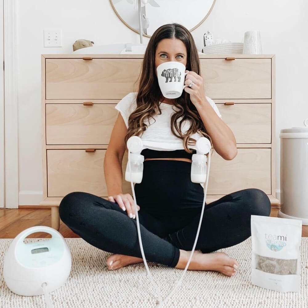 Woman drinking tea and breast pumping with pack of Teami nursing tea blend on floor next to her
