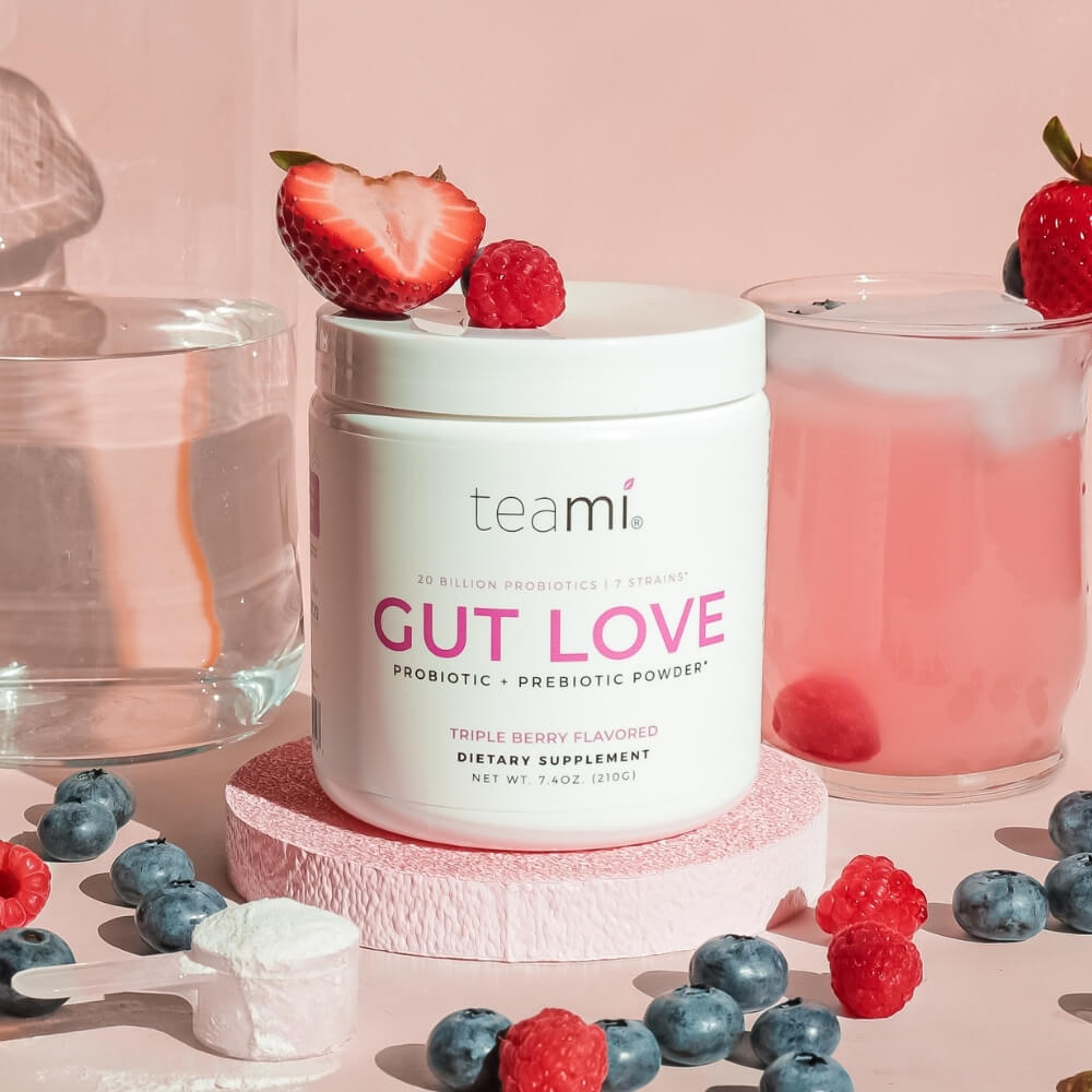 tub of Teami Gut Love triple berry flavour  surrounded by fruit on pink background