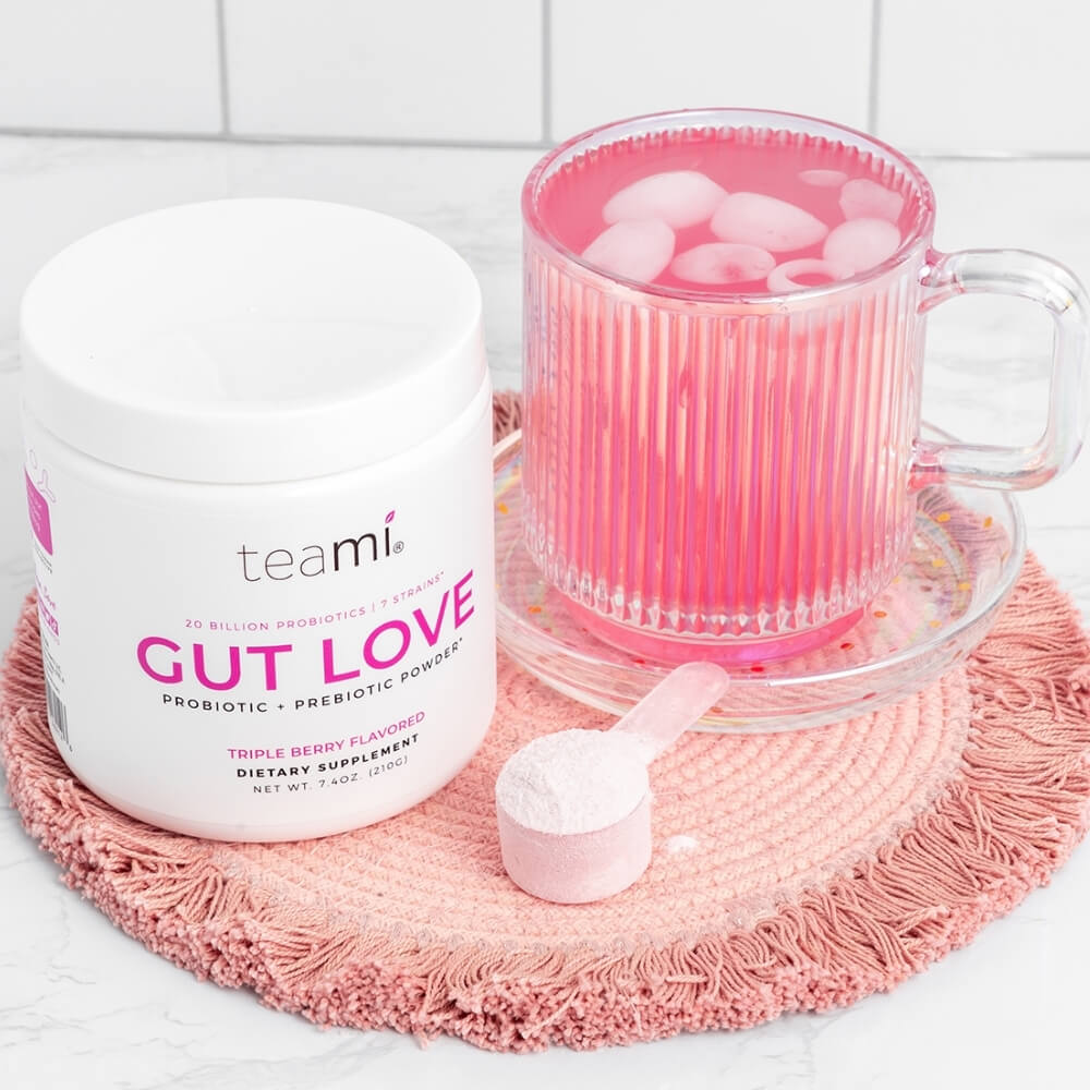 tub of Teami Gut Love triple berry flavour next to glass of drink and scoop of powder