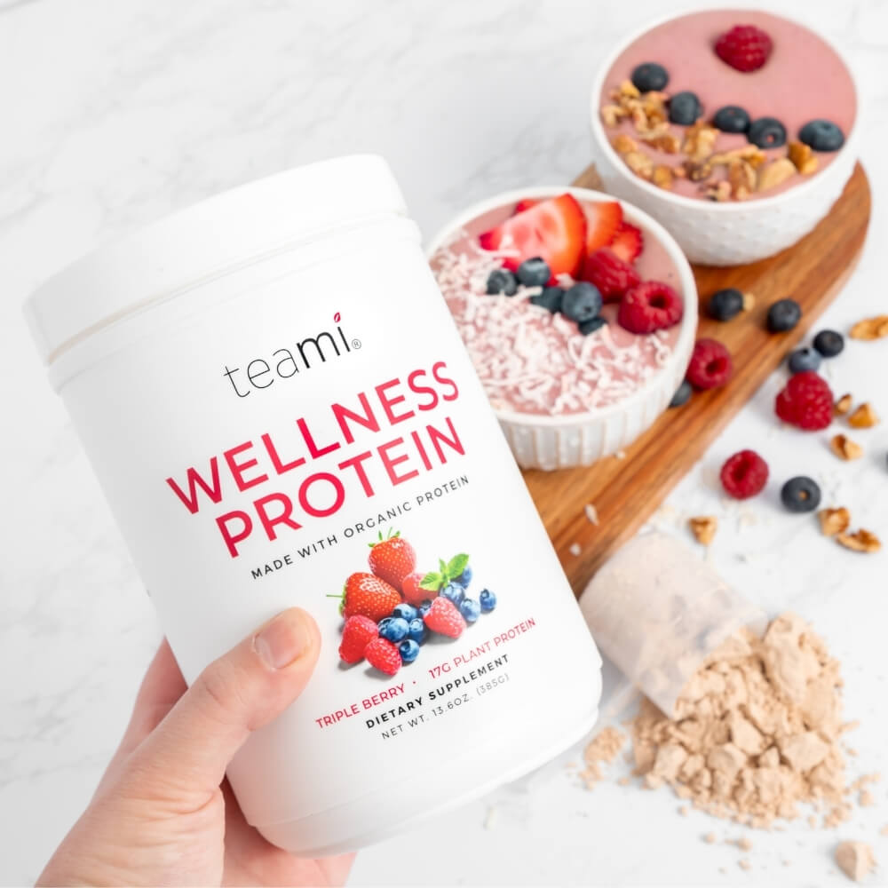 Person holding Tub of Teami wellness protein triple berry flavour