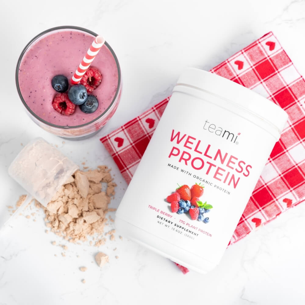 Tub of Teami wellness protein triple berry flavour lying down on kitchen surface with protein shake