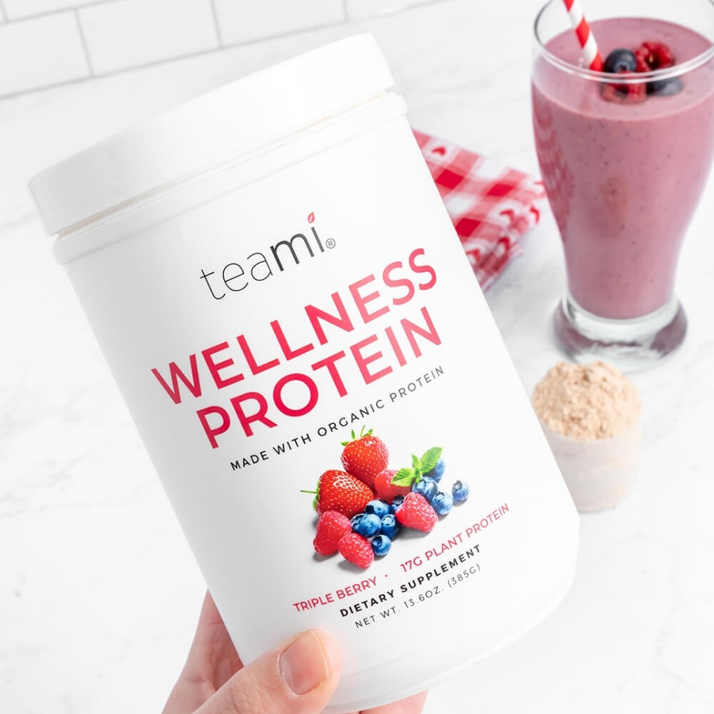 Person holding Tub of Teami wellness protein triple berry flavour