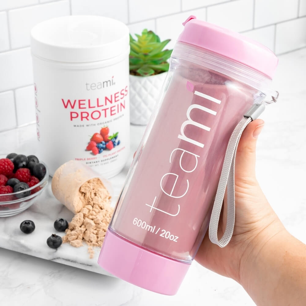 Person holding Teami tea tumbler with Tub of Teami wellness protein triple berry flavour in background