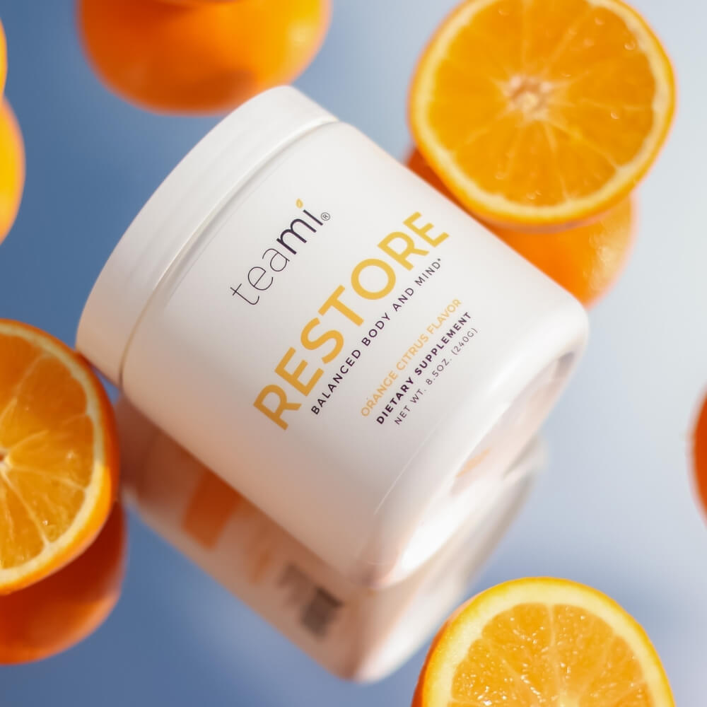 tub of Teami Restore supplement on mirror background with slices of orange fruit