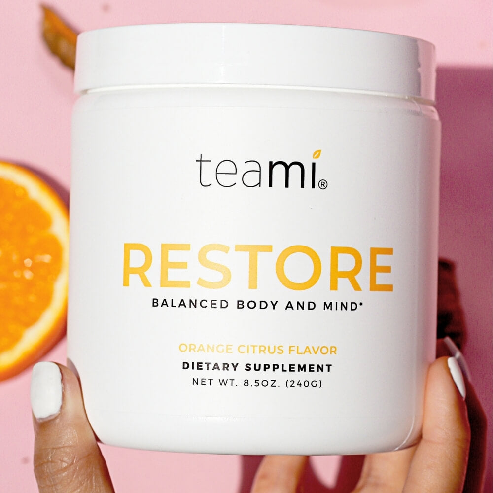Person with pink nails holding tub of Teami Restore supplement