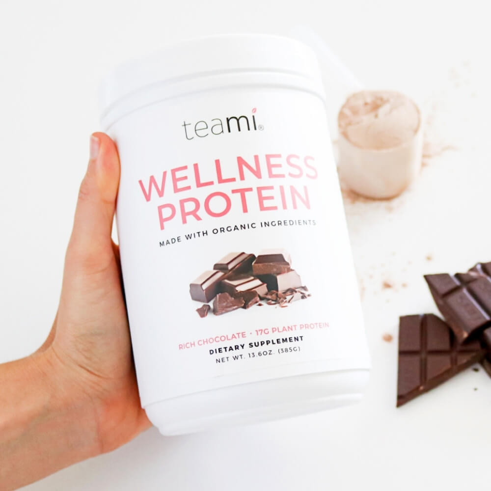 hand holding tub of teami plant based wellness protein, rich chocolate flavour