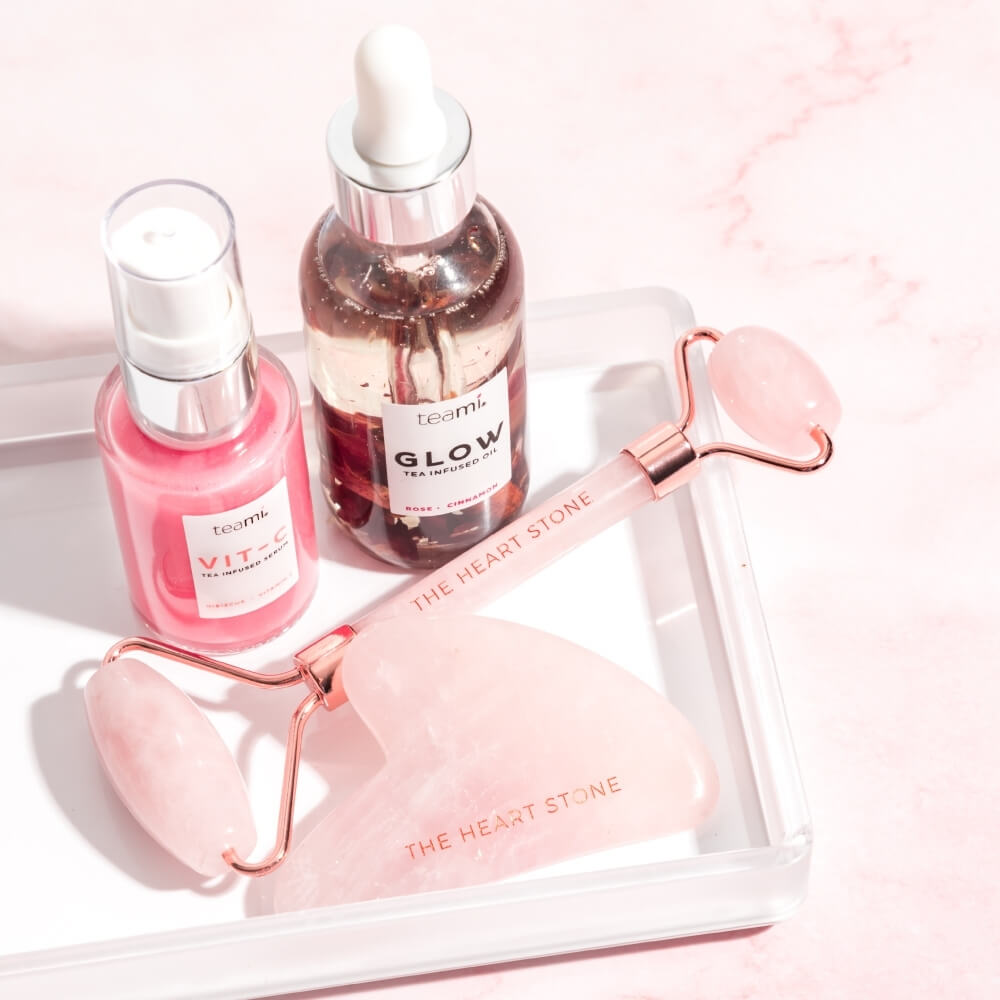 Teami Gua Sha rose quartz facial lifting tool next to facial roller, glow oil and vic c serum